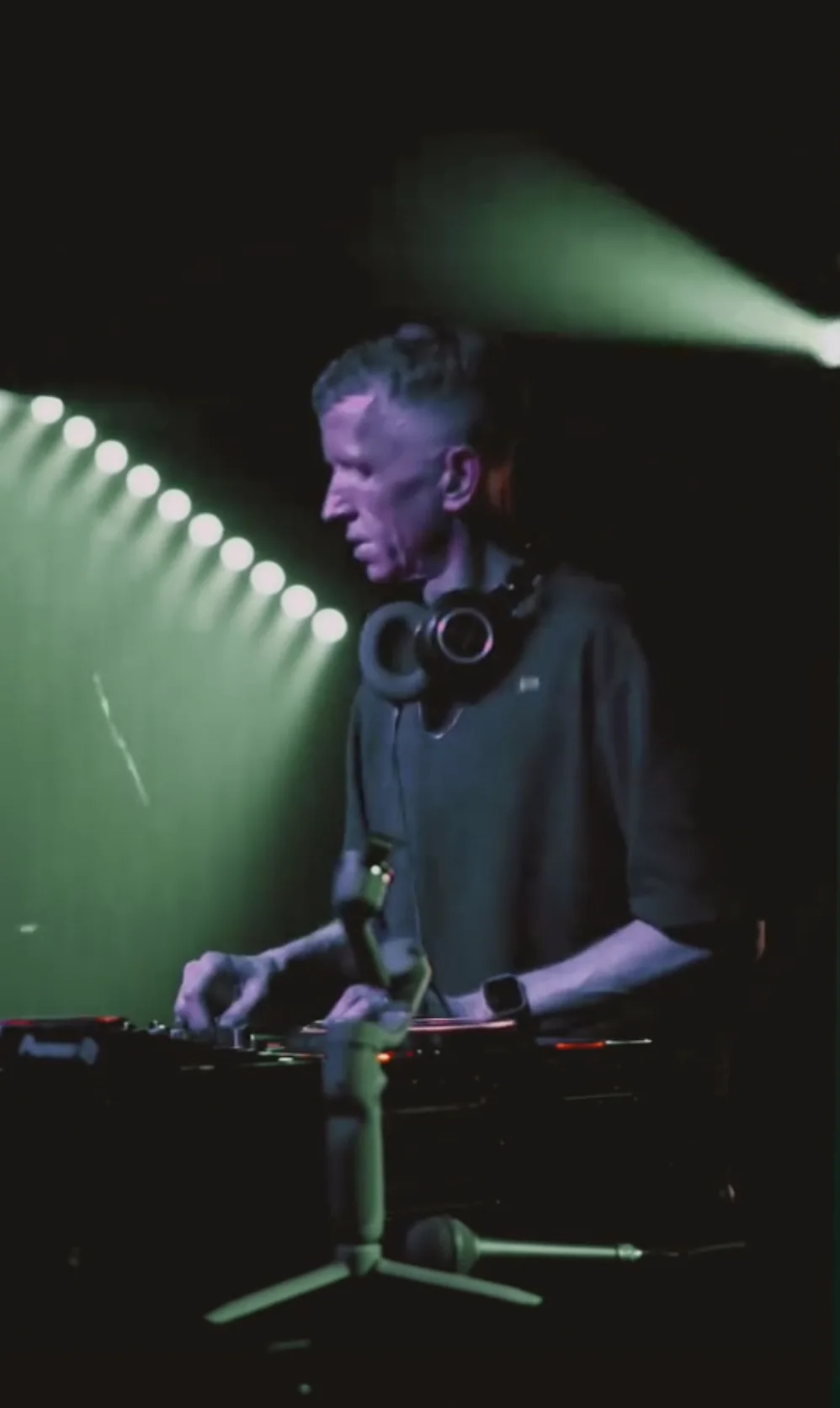 TEAK at the decks, headphones on, stage lights behind