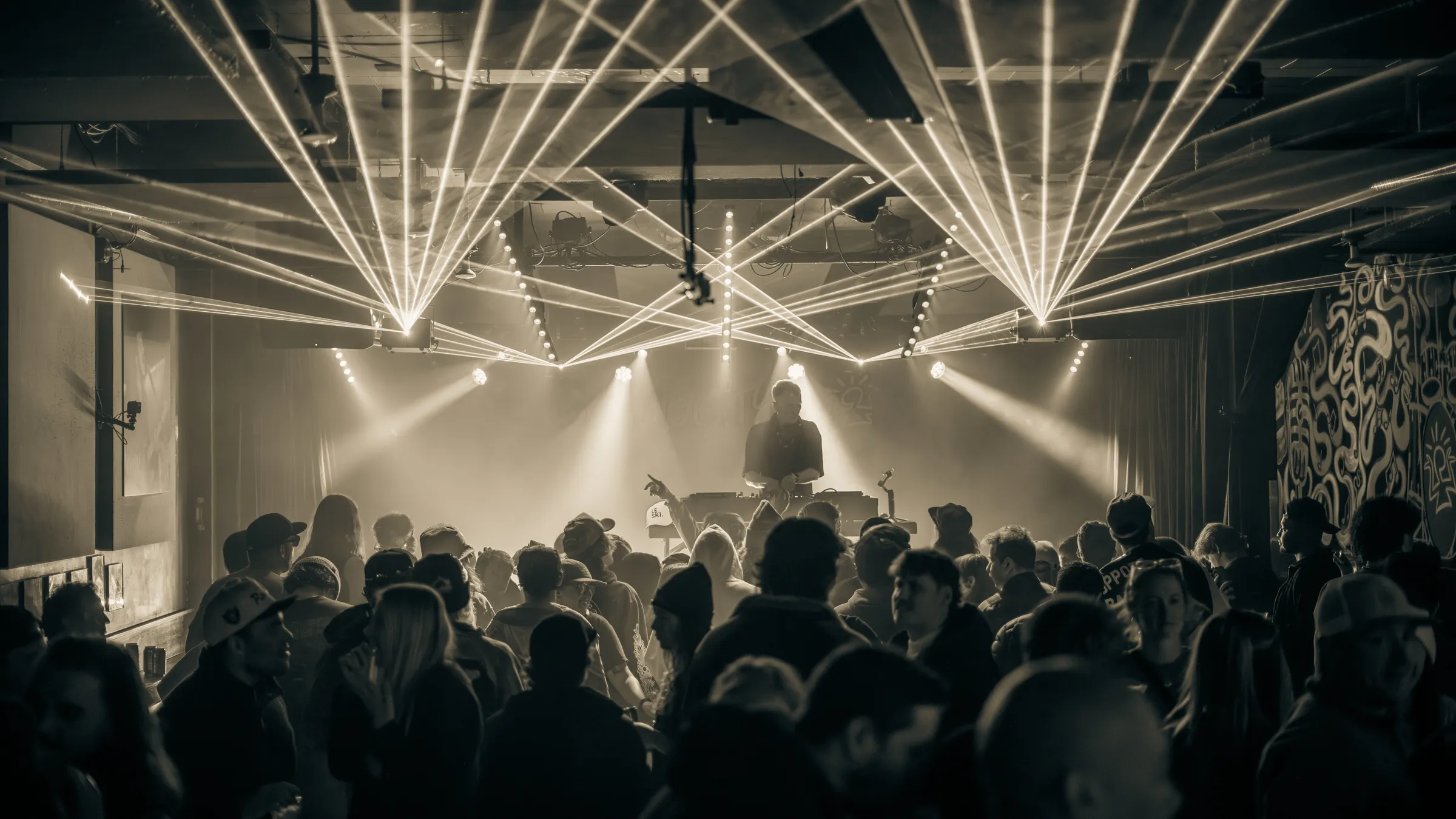 A DJ under white lasers above a packed crowd